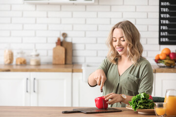 Poster - Young pregnant woman cutting bell pepper at table in kitchen