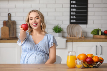 Poster - Young pregnant woman with apple at table in kitchen