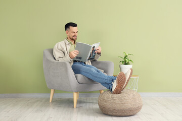 Wall Mural - Handsome man reading magazine in armchair near green wall