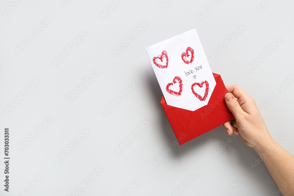 Female hand with red envelope and greeting card on grey background, closeup. Valentine's Day celebration