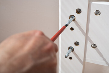 The furniture assembler assembles the bed frame, twists the fixers, hands with a close-up screwdriver