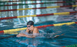 © 24K-Production - Female athlete swimming in breaststroke style in the pool lane, stroking, immersing, and lifting out of the water to breathe.