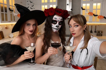 Wall Mural - Group of women in scary costumes with cocktails taking selfie at Halloween party indoors