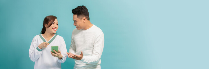 Wall Mural - Amazed attractive young Asian couple looking at smartphone together isolated on blue background