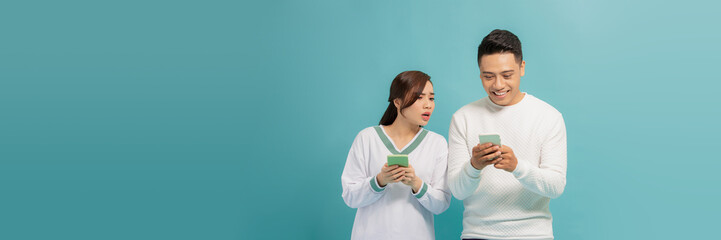 Wall Mural - Asian young girl spying on her partner's mobile phone in blue background