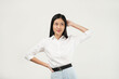 © Illhamt - An Asian woman in a white blouse adjusts her hair while smiling brightly. The plain white background enhances her cheerful and approachable vibe in a professional setting.