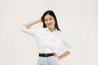 © Illhamt - An Asian woman in a white blouse adjusts her hair while smiling brightly. The plain white background enhances her cheerful and approachable vibe in a professional setting.