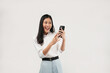 © Illhamt - An Asian woman smiles while holding a phone, exuding confidence. Captured in a bright studio, this image aims to represent connectivity and modern lifestyle choices.
