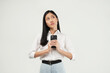 © Illhamt - A dreamy young pretty Asian woman holds a mobile phone and has a thoughtful expression thinking about the received message wears white blouse  looks away isolated white background.