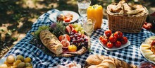 A Picnic With A Variety Of Foods On A Checkered Cloth Near An Umbrella.