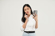 © Illhamt - Photo of young asian woman holding smartphone standing on isolated white background. She is looking at blank space and thinking something.