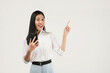 © Illhamt - Photo of young asian girl shopping on mobile app, holding phone and pointing finger left at empty copy space, showing promo text, standing with smartphone against white background