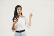 © Illhamt - Photo of young asian girl shopping on mobile app, holding phone and pointing finger left at empty copy space, showing promo text, standing with smartphone against white background