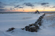 Old stone fence and a fish drying rack at the coast of the Varanagerfjord on a cold winter day during the polar night, Ekkerøya, Northern Norway