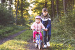 © Irina Schmidt - Cute little preschool girl in safety helmet riding bicycle. School kid boy, brother teaching happy healthy sister child cycling and having fun with learning bike. Active siblings family outdoors.