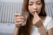 © Wanwajee - Close up of sick woman taking medicine, the pill and hand close to mouth, right hand holding glass of water.