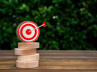 Poster - Big 3d target icon on the top of round wooden blocks stack on green natural leaves background with copy space. Business goal and success, effort and diligence, growth marketing plan concepts.
