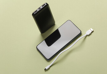 Black power bank and smartphone on green background