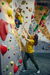 Wall Mural - Woman, bouldering trainer teaching child little girl bouldering activity, techniques. Little girl climbing wall, indoor class. Concept of sport climbing, hobby, active lifestyle, school