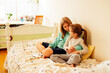 © Dasha Petrenko - Two sisters are sitting on the bed and listening to cd player. Girls share one headphones for two. Older girl takes care of younger one.