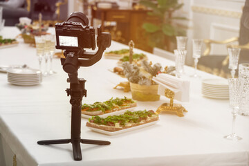 A stabilizer with a video camera on the table. buffet table with drinks and snacks. Selective focus. The concept of a coffee break for corporate and events. The work of a videographer at a wedding.