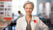 © MP Studio - Senior medical professional with white hair, wearing a lab coat , standing confidently in front of a poster displaying scientific charts and data.
