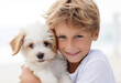 Smiling blond young boy holding a puppy dog isolated on white background looking at camera
