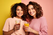 Two attractive women holding their glasses of drink on colorful background. Generative AI.