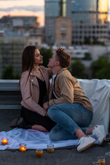 Wall Mural - Beautiful young loving couple on a surprise romantic date on a roof top. Picturesque view, skyscrapers on background. Wine, candles, kisses on holiday Saint Valentine's Day celebration outdoors