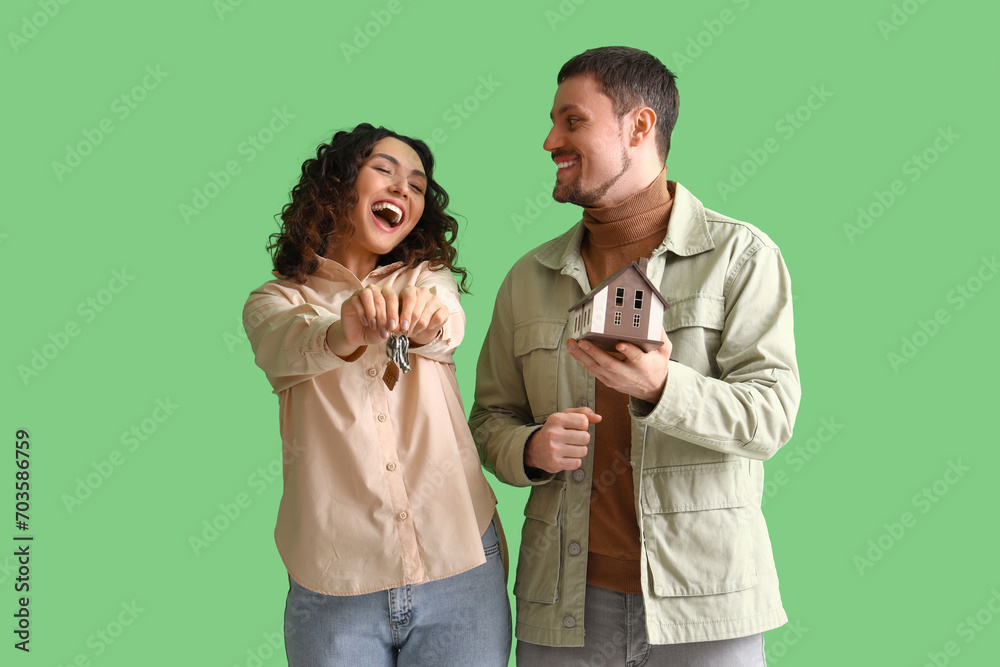 Happy young couple with house model and keys on green background