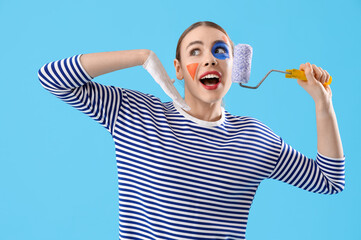 Wall Mural - Young woman with painted face and roller on blue background