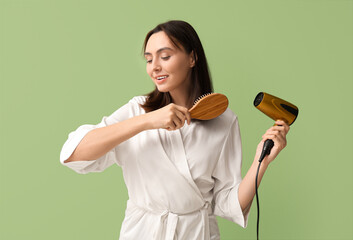 Wall Mural - Beautiful young woman with hair dryer and brush on green background