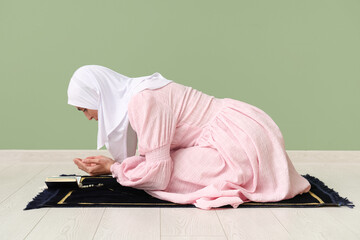 Wall Mural - Young Muslim woman praying on green background