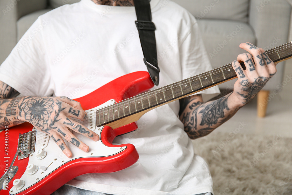 Cool tattooed young man playing electric guitar at home