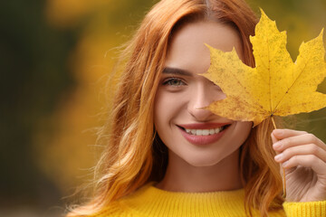 Sticker - Smiling woman covering eye with autumn leaf outdoors, closeup. Space for text