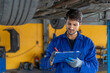 © iammotos - happy latin auto mechanic man checking tires , brakes under car with clipboard in garage cars service . hispanic technician repairing vehicle. lifted car checklist tyres and wheel in auto repair shop