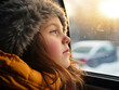 Little girl wearing in winter clothes looking out the car window, family road trip. Winter concept