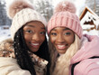 © Artem - Two black women in warm clothes look at the camera and smile against the backdrop of a winter landscape with wooden cabin