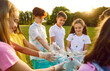 © Studio Romantic - Group of teenage volunteers children standing in a row in gloves and with garbage bags collecting plastic trash in the summer park outdoors at sunset. Cleaning environmental pollution by garbage.