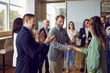 Group of a young business people standing in office and rejoicing at the deal is struck. Man shaking hands with woman finishing meeting or signing contract or greeting new employee.