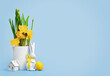Yellow Easter eggs in a nest and blooming daffodils in a white pot and Easter bunny with tiny house on blue background. Happy Easter wide web banner