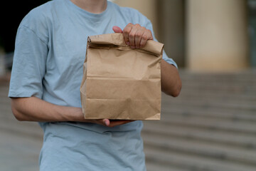 male person holding takeaway paper bag with some food outdoors