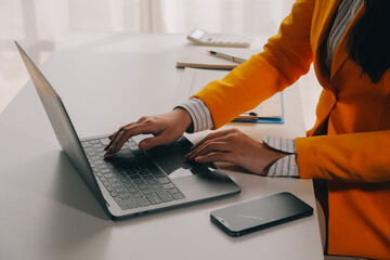 Business woman using mobile phone during working on laptop computer, surfing the internet, searching business data at modern office. Asian businesswoman online working on computer at workplace