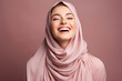 © Gonzalo - Horizontal shot of positive Muslim woman keeps eyes closed keeps hands on face smiles gladfully wears traditional hijab laughs at something funny isolated on pink background. Positive emotions concept