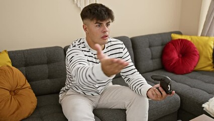 Canvas Print - Unhappy young hispanic man, sitting in comfort on sofa at home, engrossed in serious gaming on internet, using joystick of his gadget; attractive gamer visibly upset while playing video game indoors