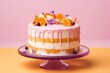  a cake sitting on top of a cake plate covered in icing and fresh fruit on top of a purple cake stand on a yellow table with a pink background.
