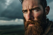Portrait of a man with a rugged beard and intense gaze, standing against a backdrop of a stormy sky