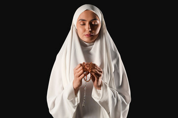 Wall Mural - Young Muslim woman with beads praying on black background