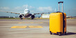 Yellow plastic travel suitcase on an airport runway with an airplane in the background. Summer vacation and tourism concept.