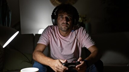 Poster - Intense young hispanic man playing video games in a dark living room, showcasing entertainment and modern lifestyle.